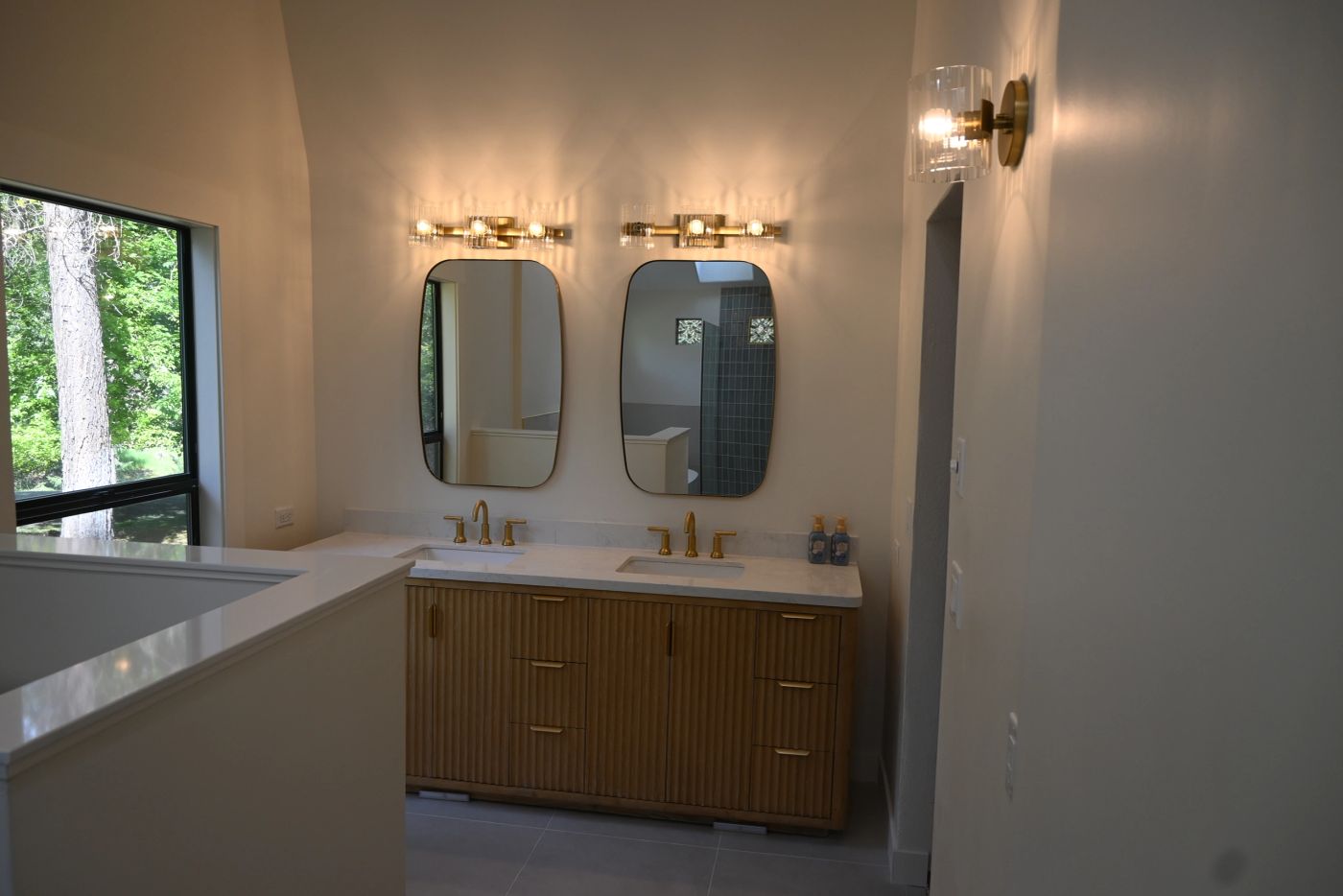 Completed bathroom with wood vanity, twin mirrors, and brass fixtures