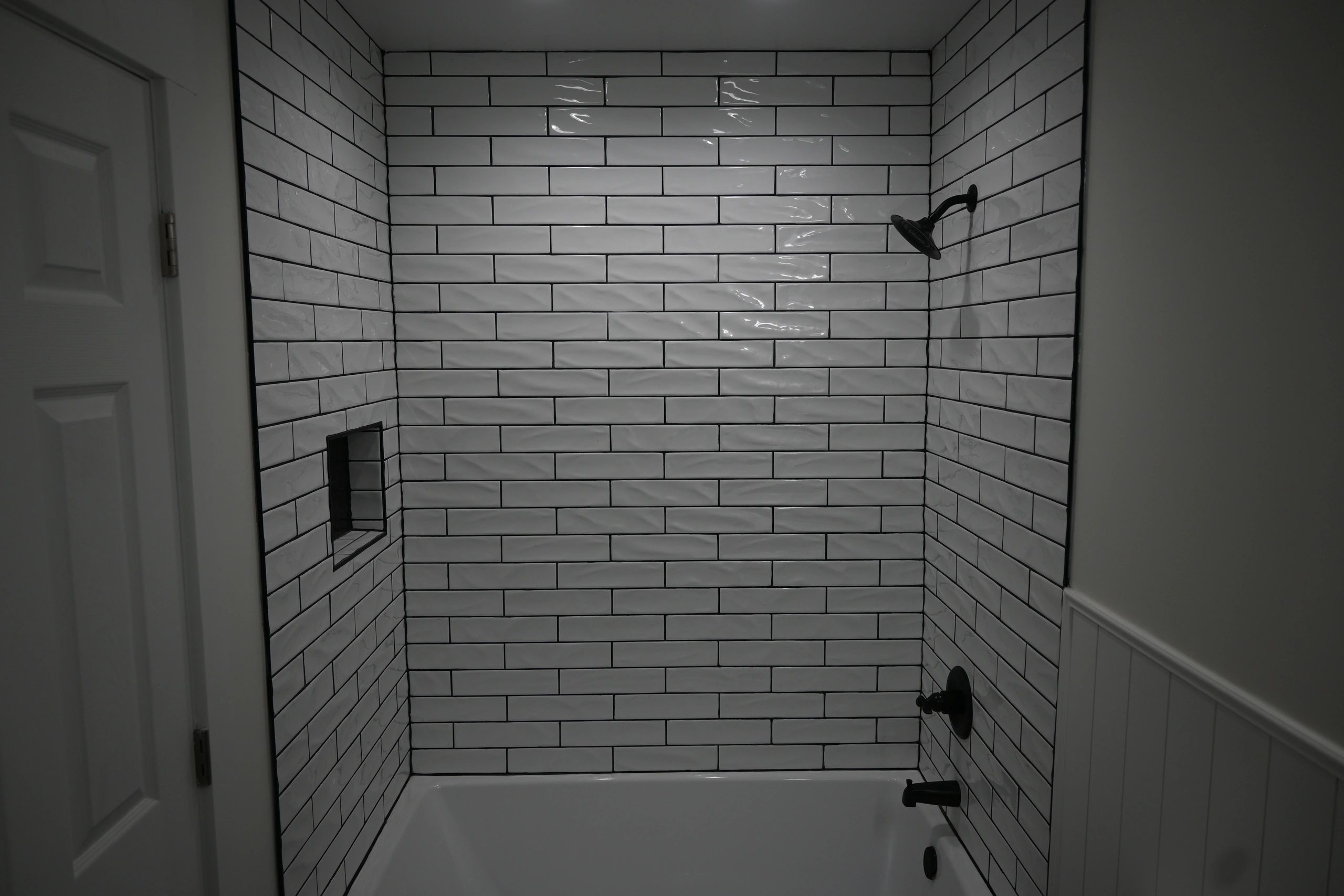 Walk-in shower with white tile, black fixtures, and a glass enclosure