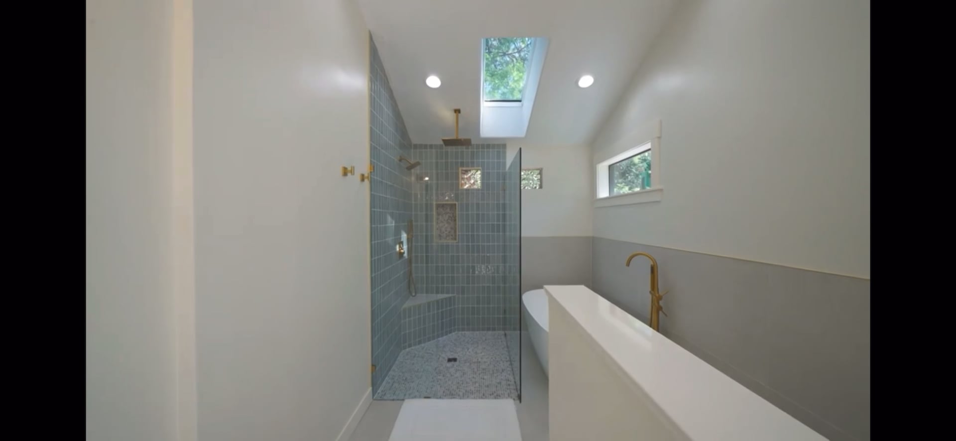 Bathroom with a blue tile shower, skylight, freestanding tub, and brass fixtures